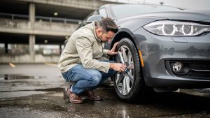 Un homme vérifie les pneus et les feux d’une voiture garée dans un parking avant un contrôle technique.