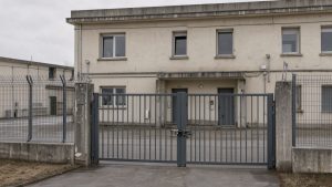 Façade sobre d’une maison d’arrêt française avec portail sécurisé, clôtures renforcées et bâtiment administratif, photographiée dans une ambiance documentaire réaliste sans personne identifiable.